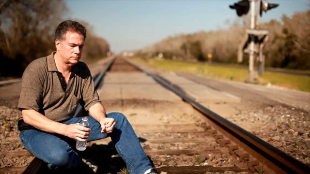 A man sitting on a railroad track drinking some water.