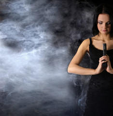 Fototapeta na wymiar Attractively looking woman with a gun on a smoky background