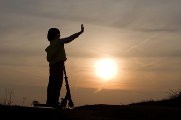 silhouette of little girl with the scooter in sunset