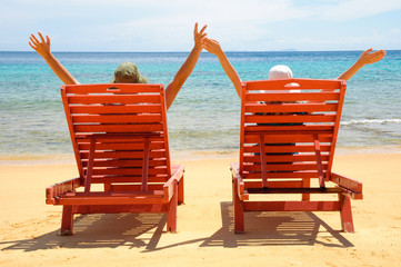 A couple resting by the beach on a red sun chair