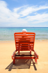 A woman resting by the beach on a red sun chair