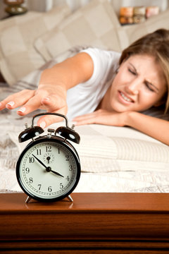 Young woman couch in the bed and turning off the alarm clock