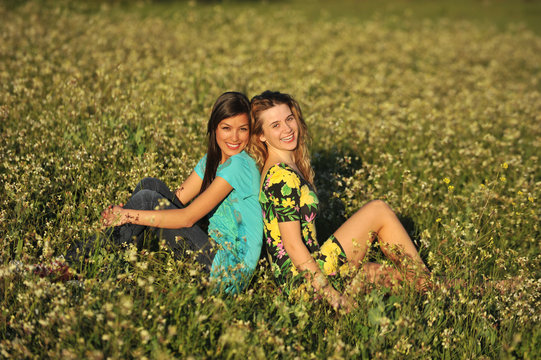 Two beautiful young women sitting in meadow