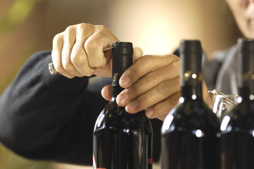 mani da uomo che stappano una bottiglia di vino rosso
