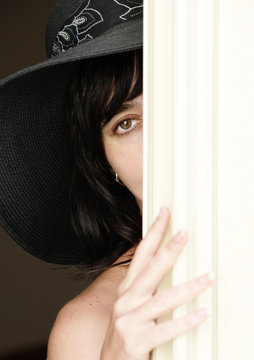Beautiful brunette woman in hat looking fro behind a curtain