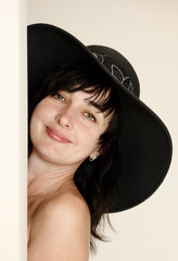 Beautiful brunette woman in hat looking from behind a corner