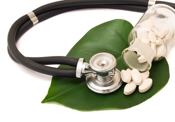 Pills, bottle and stethoscope on the leaf.
