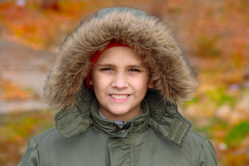 The smiling boy in a hood on a background of an autumn forest