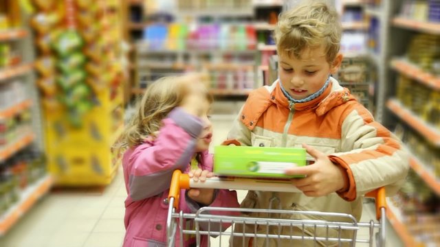 boy and girl with shopping trolley looks at box in supermarket