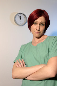 Eine Frau als Pflegekraft im medizinischen Bereich wirkt durch Überstunden übermüdet und die Uhr zeigt fünf vor zwölf