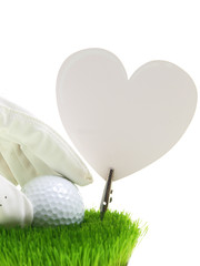 Hand mit Golfhandschuhen hält einen Golfball auf dem Rasen, wo ein großes weißes Papierherz steht