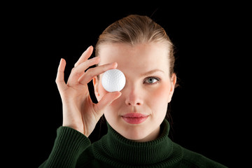 woman in a green turtleneck holds one golf ball in front of her