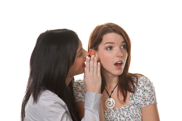 Two young women whisper to each other