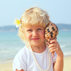 pretty little girl has lean seashell bowl to an ear on seacoast