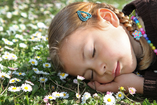 Young girl sleeping amongst daisies in a meadow