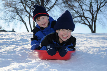 Two young boys sledding downhill together