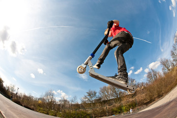boy jumping with a scooter over a funbox