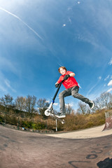 boy jumping with a scooter over a funbox