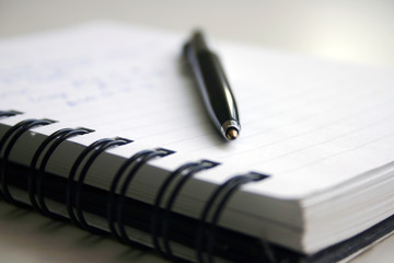 A black pen and notebook with blur background.