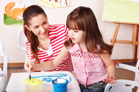 Child with teacher draw paints in play room. Child care.