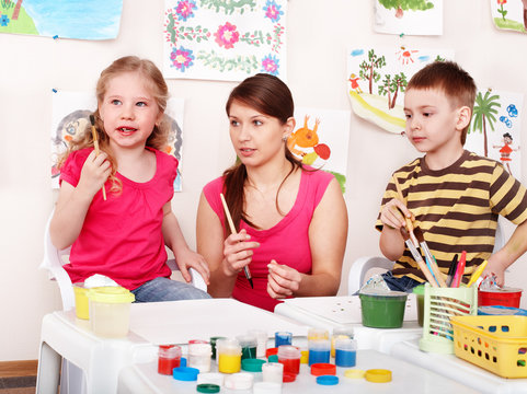 Children with teacher draw paints in play room. Preschool.