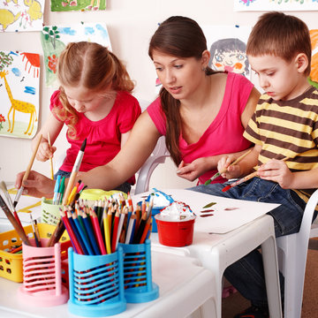 Children with teacher draw painting in play room. Preschool.