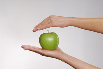 Manos protegiendo una manzana verde.