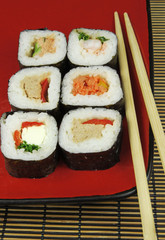 sushi futomaki on red plate with chopsticks