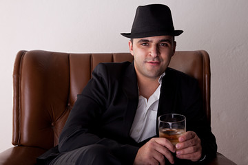 Man with hat seated on a chair, with a glass of whiskey