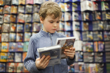 boy chooses one of two dvd in special store, ready contents - obrazy, fototapety, plakaty