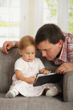 Father and toddler reading book on sofa