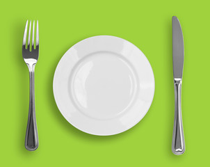 Knife, white plate and fork on green background