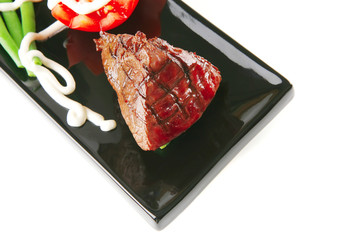 fillet mignon on a black plate with tomato