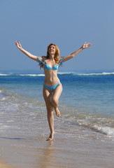 Fototapeta na wymiar Young graceful woman goes on coast of ocean