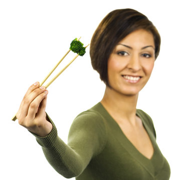 Smiling young woman holds a piece of green broccoli with chopsti