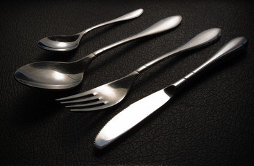 shiny cutlery set on black leather background