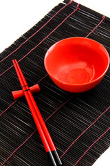 Red bowl and chopsticks (against a bamboo background)