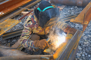 welder in protective mask welding metal construction on open air