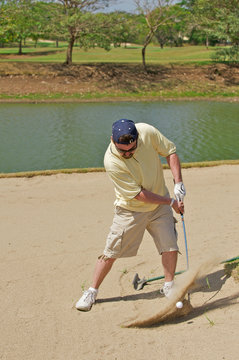 Golfer hitting the golf ball out of a sand hazard.