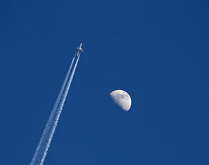 Jet mit Kondensstreifen passiert Mond an klarem blauem Himmel