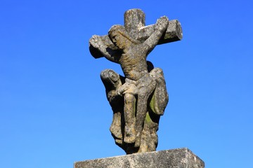 Jesus Christus am Kreuz, Steinfigur vor blauem Himmel