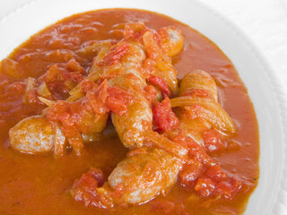Sausages in tomato sauce on white dish.