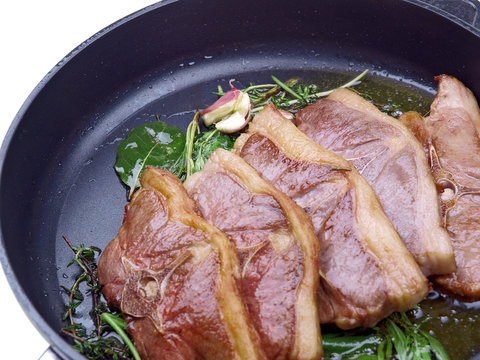 saddle of lamb, garlic & herbs roasting in a pan
