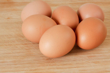 Six brown eggs on wooden board.
