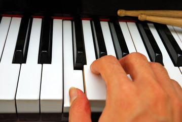 Right hand playing on piano keyboard with drum sticks