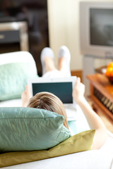 Fototapeta na wymiar Blond woman using a laptop lying on a sofa