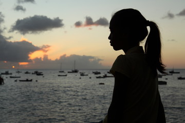 Silhouette of young girl with pony tail by sea at sunset