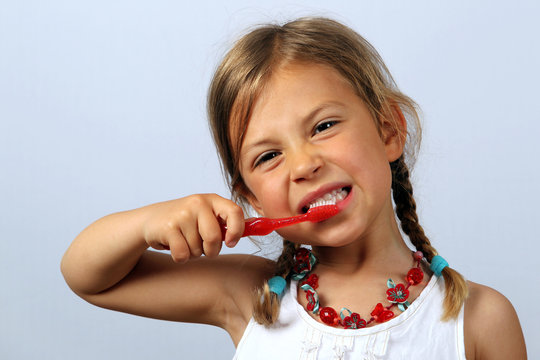 Liitle girl brushing her teeth vigorously with a red toothbrush
