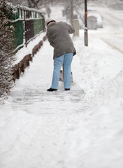 Woman shoveling snow from the sidewalk in front of his house aft