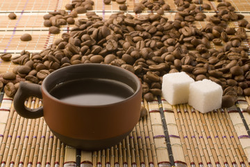 A cup of coffee and sugar cubes surrounded by coffee beans